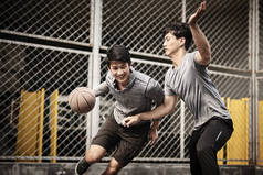 两名年轻的亚洲成年男子在室外场地上一对一地打篮球
