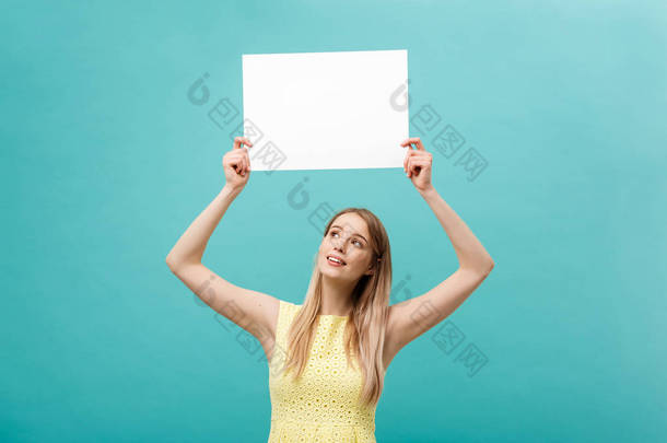 <strong>肖像</strong>美丽的年轻白种女人拿着一张空白纸, 在柔和的蓝色背景下隔离