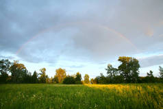夏景戏剧化的云彩在黄昏的草地上，彩虹在雨后