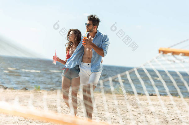 情侣在吊床附近的海滩上散步酒精鸡尾酒