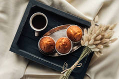 顶部的咖啡和松饼在托盘上与 lagurus ovatus 花束的米色布, 早餐在床上的概念