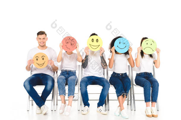 多民族朋友坐在白色的 t恤上, 坐在椅子上, 拿着在白色上被隔离的五颜六色的标志