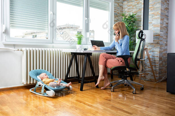 有爱心的母亲坐在<strong>办公</strong>桌前，婴儿躺在地板上，这是母亲孩子的概念