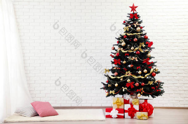 <strong>圣诞树</strong>，附有装饰品和礼品盒，矗立在<strong>白色</strong>砖墙附近的家中