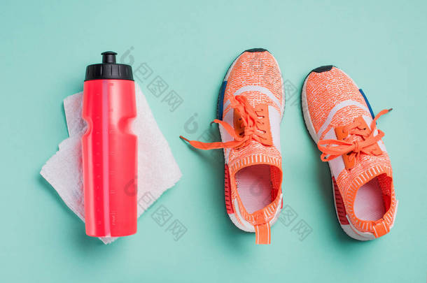 在绿松石背景下的运动鞋, 运动瓶和毛巾的顶部视图