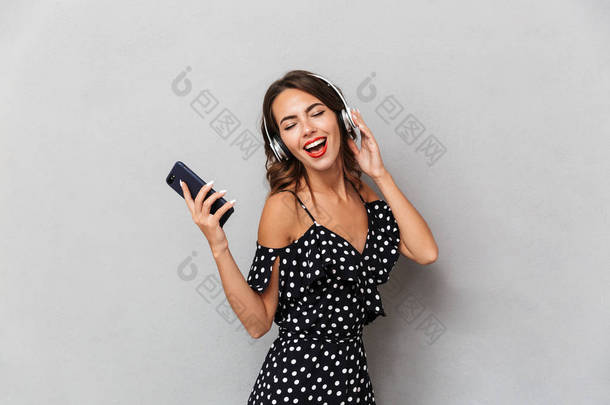 一个快乐的年轻女孩的肖像在灰色背景下, 听音乐与耳机