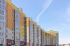 在蓝天的背景上俯瞰一座新的多层楼房。大楼的墙壁漆成橙色、红色和白色