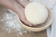 两个手拿着面包面团，盖在木制桌子上的一个防腐篮子上，用面粉和厨房毛巾