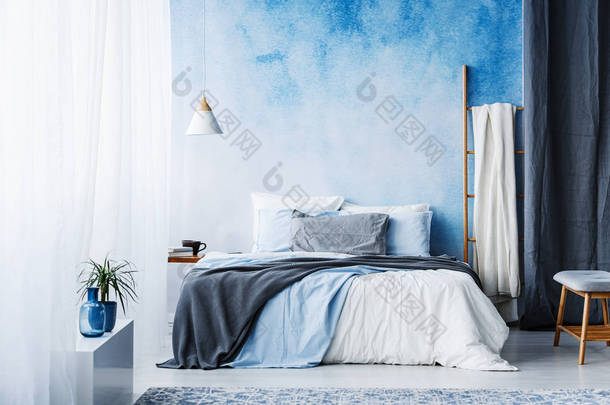 在宽敞的卧室内有梯子和植物的灰色和蓝色床上用品