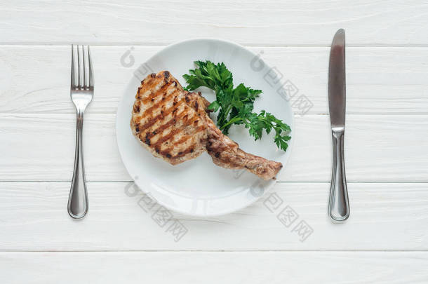 在白色木制背景的欧芹和餐具盘上的美味肋骨<strong>眼肉牛排</strong>的顶部视图