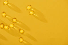 金光闪闪的鱼油胶囊分散在黄色明亮的背景上，有复制空间的顶部视图