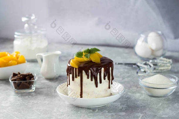 厨房的白桌上放着一个白色的蛋糕，上面涂满了巧克力和切碎的桃子。做蛋糕的配料是相邻的