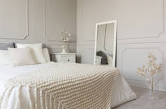 米色羊毛毯子在白色床上用品的特大号床在时尚的卧室内部与灰色墙壁