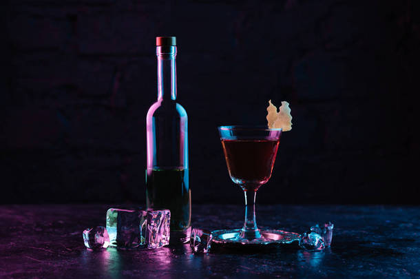 一杯酒精鸡尾酒, 一瓶酒和冰块在黑暗的表面上