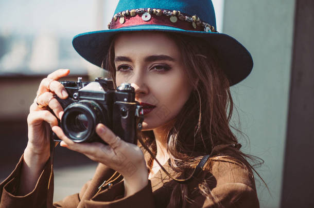戴帽子的优雅女人在屋顶上的复古摄影相机上拍照