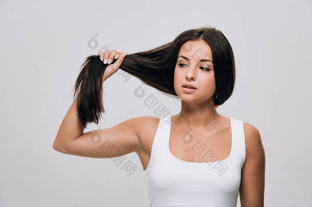 黑发美女看着长直健康和闪亮的头发隔离在灰色