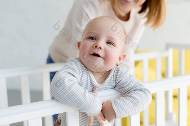 小微笑的儿子在婴儿床与母亲后面