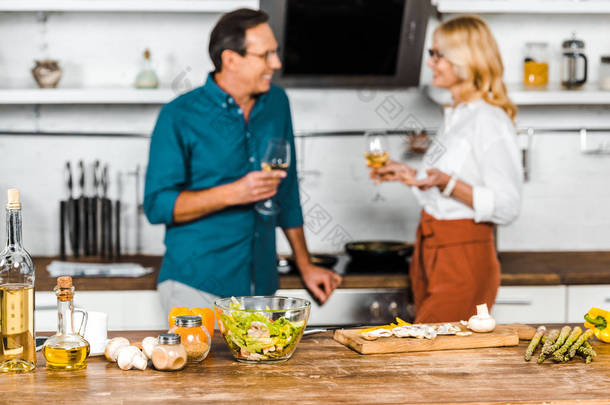 有选择的焦点成熟的妻子和丈夫拿着一杯葡萄酒, 并在厨房里看着对方