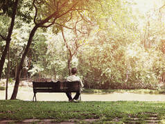 在日出的公共公园的木凳上, 孤独的老人 siiting 的背观。老式滤镜效果.