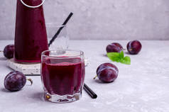 红色李子汁在玻璃杯的灰色石头背景与新鲜的水果。有选择的重点.