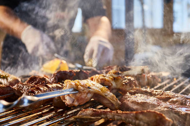 肉用<strong>格子</strong>烤架、排骨、木桩、香肠、边、鸡、明火、黑胡椒、烟、柴火、厨师手拿肉、手拿着手套、关门