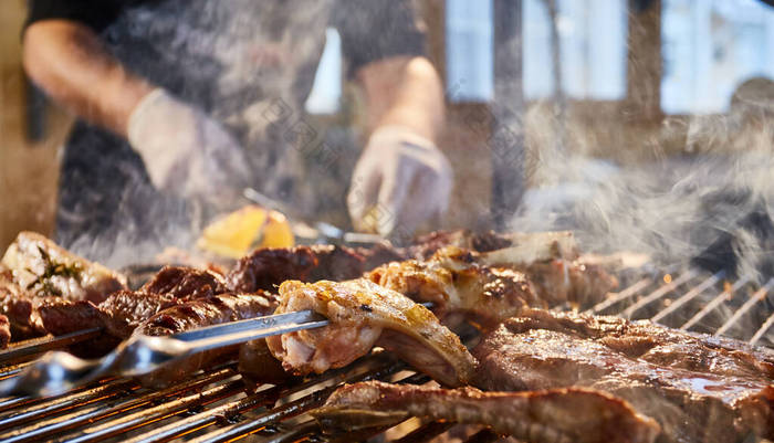 肉用格子烤架、排骨、木桩、香肠、边、鸡、明火、黑胡椒、烟、柴火、厨师手拿肉、手拿着手套、关门