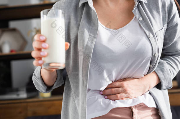 患有乳糖不耐受症的妇女在触摸胃时举着一杯<strong>牛奶</strong>的剪影 