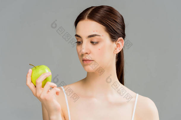 年轻女子与痤疮看着绿色苹果隔离在灰色 