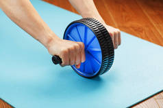 运动用蓝色卷轴训练双手的腹肌.一个人在健身房或家里参加体育活动.