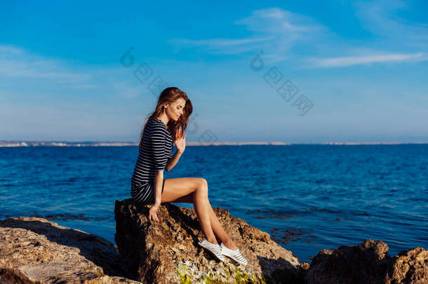 穿条纹连衣裙的女孩坐在海边岩石上