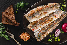 用调料、青菜和面包片包裹在深色石质背景上的腌制鱼片或鱼片鲱鱼。地中海食物，开胃菜，海鲜，顶级风景