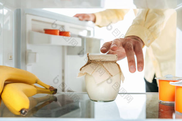 从被白色隔离的打开的冰箱中取出酸奶油的照片
