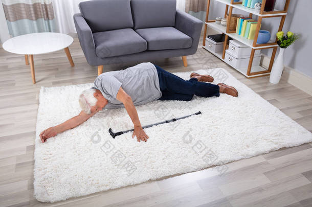 无意识的高级男子与拐杖躺在地毯在家里