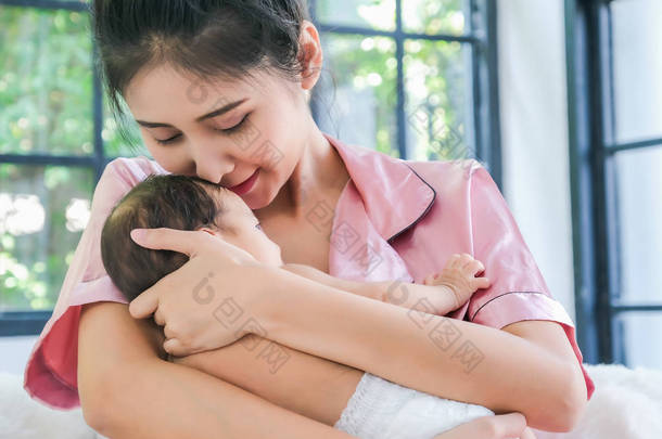 亚洲母亲抱着<strong><strong>一</strong>个</strong>1.5个月大的孩子，靠在她的sho