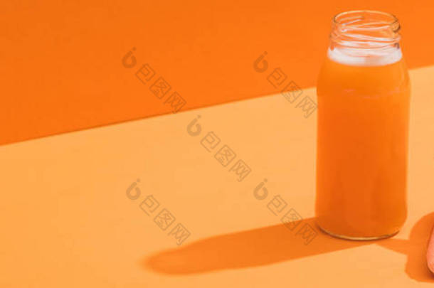 橙底成熟胡萝卜附近的玻璃瓶中的新鲜果汁，全景拍摄