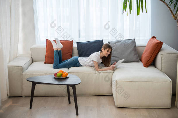 女青年卧在沙发上的侧面观与现代室内的数码片使用