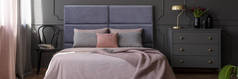 粉红色的床单上的大床与软床头站在黑暗的卧室内金色的灯和新鲜的郁金香在灰色橱柜