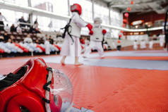 红色战斗头盔与清晰的塑料面罩在地板上在前景。两个男孩在和服的背景空手道战斗