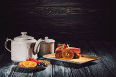 胡萝卜蛋糕在盘子, 橙色切片, 蓝莓和小红莓在木桌茶壶附近的茶托上