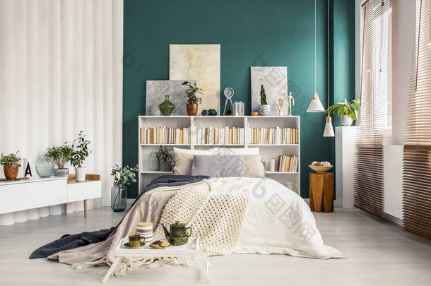 <strong>书柜</strong>床头板与艺术品和装饰在一个时尚的绿松石绿色卧室内饰与白色家具
