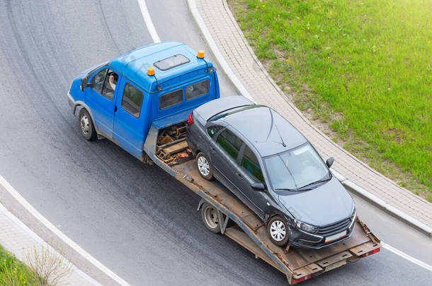 车祸中车轮破碎的客车被装上了一辆疏散卡车，沿着公路行驶，然后转上公路，从空中俯瞰