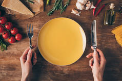 用刀叉在盘子上切下的手, 在木桌上放着一排面食和新鲜的配料