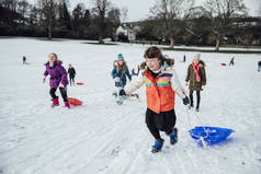 一群小女孩在雪地上跑了一个小山, 有一个雪橇比赛.