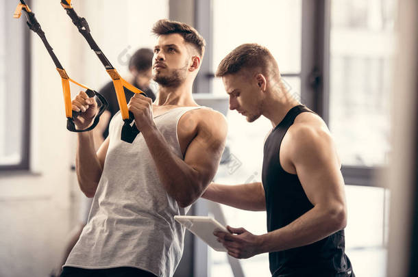 训练员使用数字片和帮助<strong>肌肉</strong>运动员锻炼健身带在健身房
