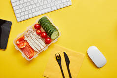 午餐盒的顶视图与蔬菜和鸡肉在黄色背景与计算机键盘
