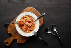 在木制切菜板上，在黑色木制背景的餐具旁边，可以俯瞰美味的番茄酱番茄酱意大利面食