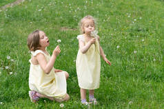 两个女孩在绿草地上，蒲公英站在黄色礼服