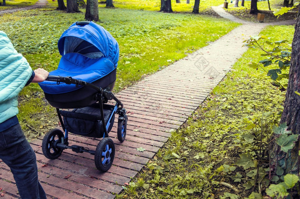 在公园里, 一辆婴儿车在绿树成荫的背景下漫步。色调照片