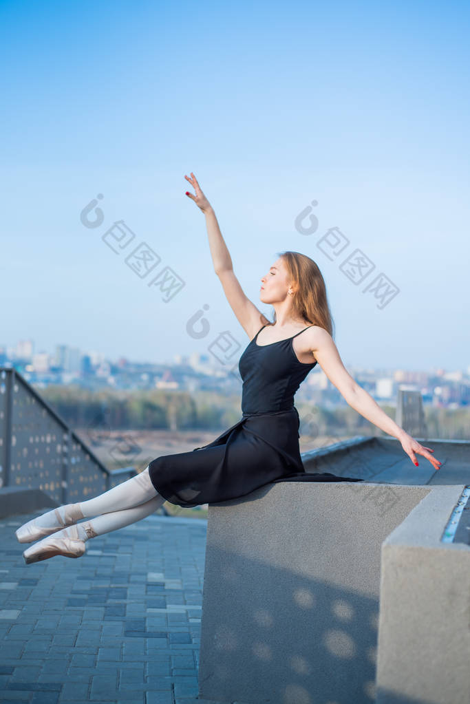 芭蕾舞在图图冒充坐。美丽的年轻女子在黑色礼服和点跳舞的城市背景。华丽的芭蕾舞表演在户外跳舞的肖像