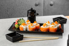 费城卷寿司与鲑鱼，鳄梨，奶油奶酪和红色鱼子酱。 寿司菜单。 在黑暗的盘子里 日本传统海鲜,健康食品的概念. 白色背景的俯瞰水平照片.